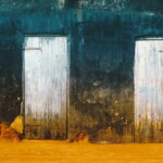 Zwei verwitterte weiße Holztüren in einer verfallenen blau-orangen Hausfassade – Symbolbild für den Unterschied zwischen Auszahlung und Ausgabe im Rechnungswesen.