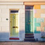 Zwei Haustüren in Hellgrün und Petrol neben einer bunten Patchwork-Fassade – Symbolbild für den Unterschied zwischen Ertrag und Leistung im Rechnungswesen.