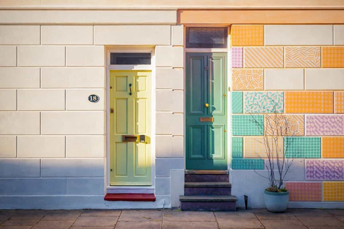 Zwei Haustüren in Hellgrün und Petrol neben einer bunten Patchwork-Fassade – Symbolbild für den Unterschied zwischen Ertrag und Leistung im Rechnungswesen.
