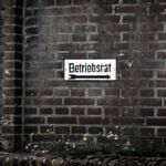 Abmahnung Betriebsrat / Hinweisschild „Betriebsrat“ an Backsteinwand mit Pfeil nach rechts und Hausnummer 145