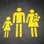 Gelbes Piktogramm einer Familie mit Kind auf Asphalt – Symbol für Mutterschutz, Elternzeit und Pflegezeit