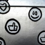 Personalrecruiting (Graffiti mit sozialen Medien-Symbolen, darunter ein Herz, ein Smiley und ein Daumen-hoch-Zeichen, auf einer silbernen Wand.)