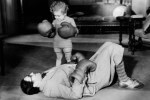 K.o.-System / K.o.-System symbolisch dargestellt: Kind mit Boxhandschuhen knockt einen Erwachsenen aus