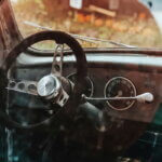 Management & Controlling: die 10 Top-Beiträge 2018 / Innenansicht eines alten Autos mit nostalgischem Lenkrad und Armaturenbrett, durch die leicht verschmutzte Scheibe fotografiert, im Hintergrund verschwommene Herbstdekoration.