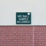 Google Penaltys / Abgenutztes Schild an einer Mauer mit der Aufschrift „No ball games allowed“ (Keine Ballspiele erlaubt).