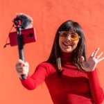 Influencer Marketing (Brunette girl smiling and waving while recording a video blog with the mobile phone and microphone, wearing a dress for social networks.)