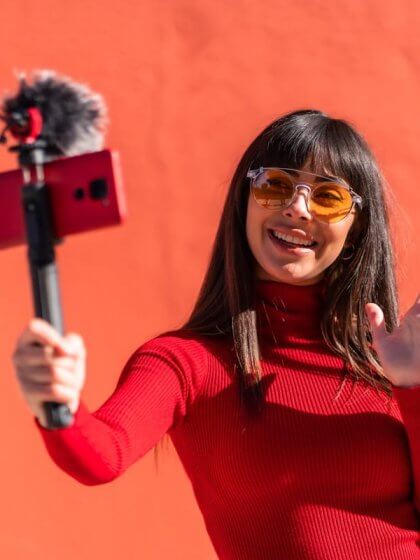 Influencer Marketing (Brunette girl smiling and waving while recording a video blog with the mobile phone and microphone, wearing a dress for social networks.)