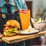 Bewirtungskosten (Mann serviert Burger und Getränk)