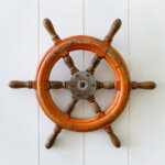 Steuerpflicht (Old boat steering wheel mounted on the white wall)