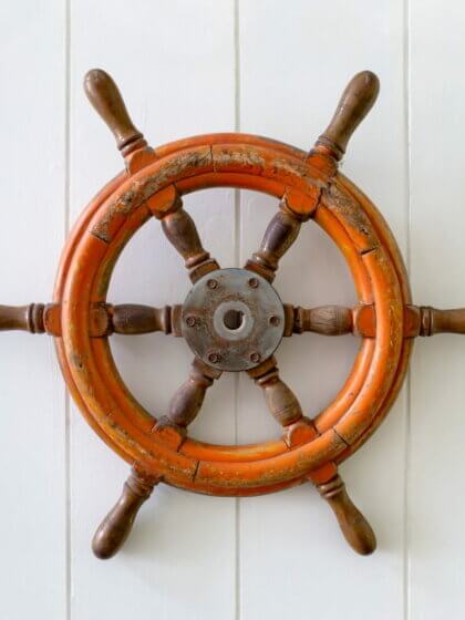 Steuerpflicht (Old boat steering wheel mounted on the white wall)