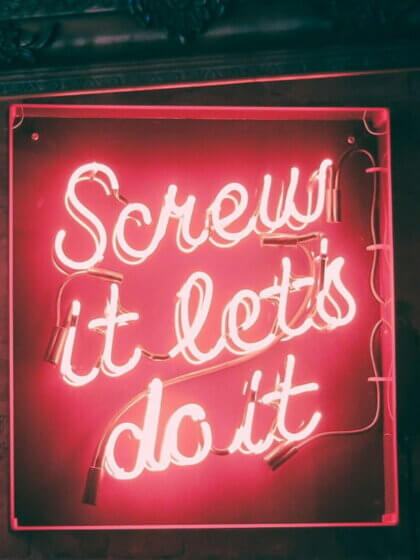 Umsatzsteuer-Voranmeldung (Neon-Schriftzug in Pink mit der Aufschrift „Screw it, let’s do it“, eingefasst in einen dekorativen Rahmen, vor einer dunklen Wand.)