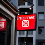 Internetfreiheit, Internetzensur (Leuchtendes rotes Schild mit der Aufschrift „Internet @“ an der Außenwand eines Gebäudes, im Hintergrund Fenster einer Stadtfassade.)