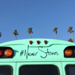 Stressmanagement (Mintgrüner Bus mit der Aufschrift „#NeverStress“ auf der Rückseite, dahinter ragen Palmen vor einem klaren blauen Himmel empor.)