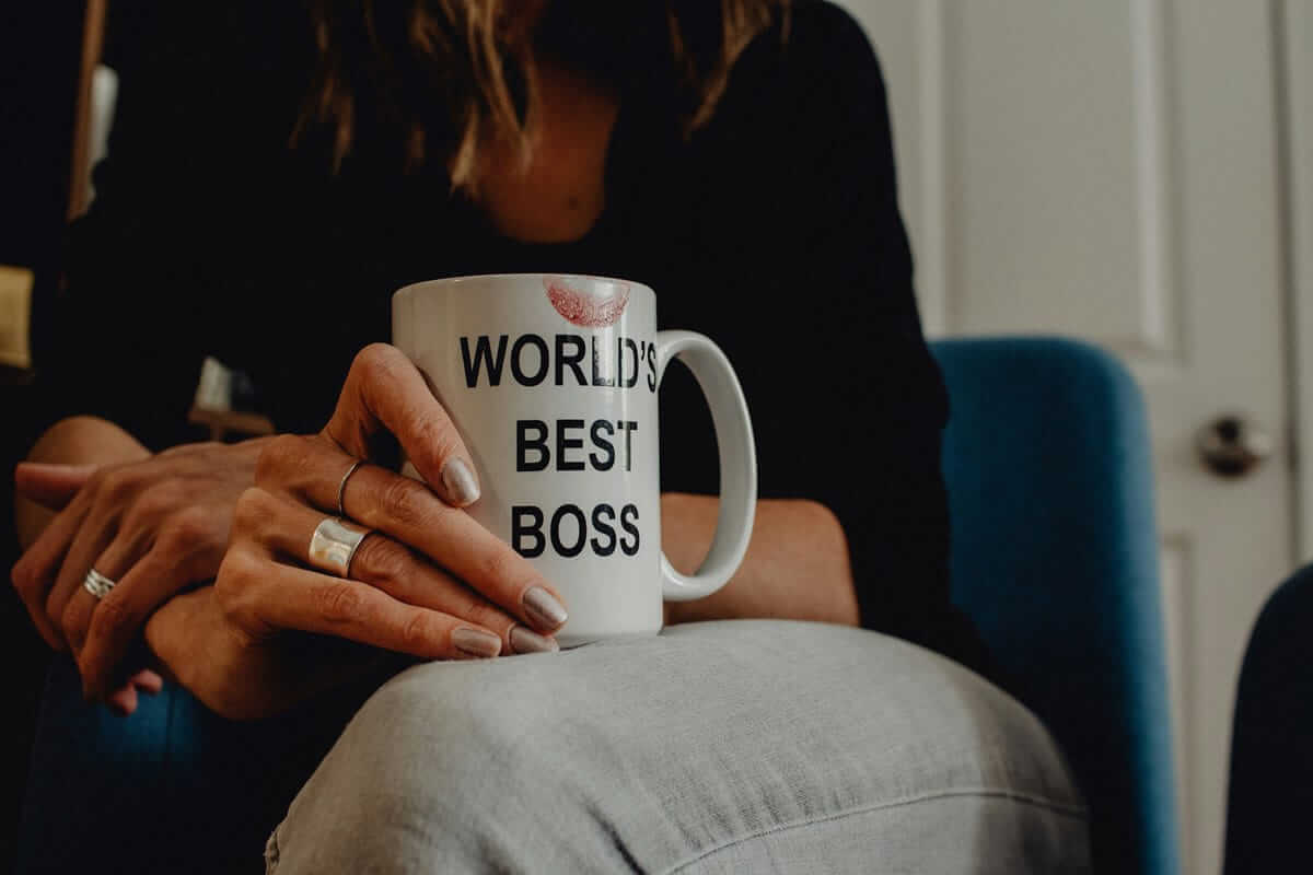 Führungsqualität Frauen / Frau mit Tasse „World’s Best Boss“ in der Hand, Lippenstiftabdruck sichtbar – Symbolbild für weibliche Führung und moderne Leadership-Qualitäten