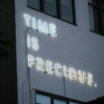 Stundensatz / Leucht-Schriftzug „Time is precious“ an einer Häuserwand – Symbol für den Wert von Zeit und die Bedeutung realistischer Stundensätze.