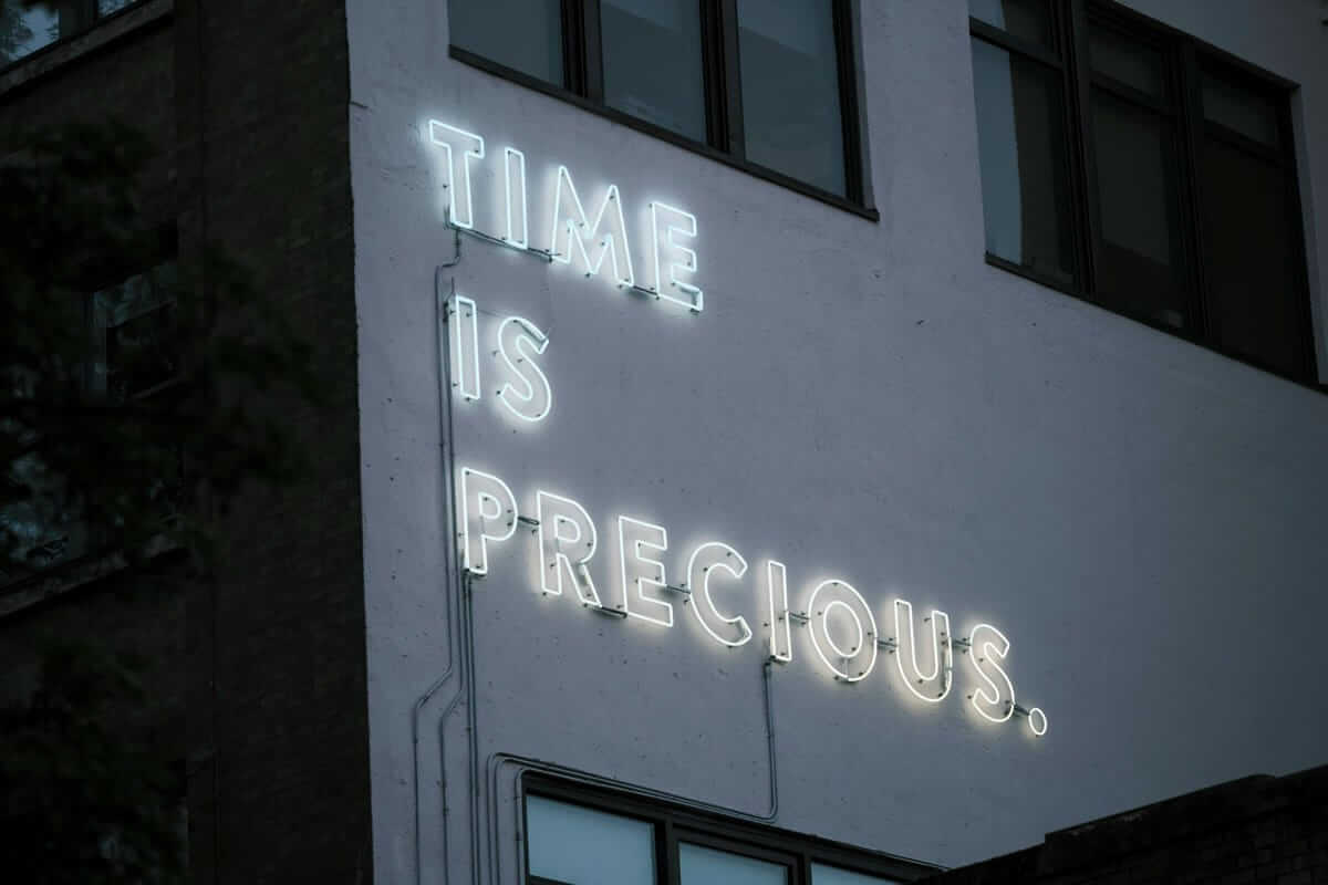 Stundensatz / Leucht-Schriftzug „Time is precious“ an einer Häuserwand – Symbol für den Wert von Zeit und die Bedeutung realistischer Stundensätze.