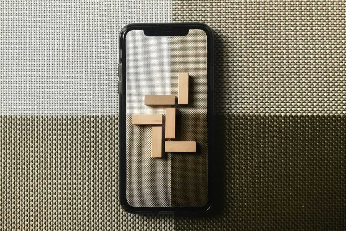 Handy am Arbeitsplatz / Smartphone auf gemustertem Untergrund mit kleinen Holzklötzen darauf – symbolische Darstellung für Struktur und Regeln bei der Handynutzung