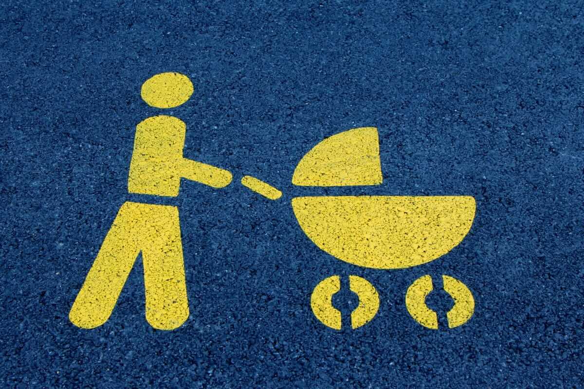 Gelbes Piktogramm einer Person mit Kinderwagen auf Asphalt – Symbol für Elternzeit und Elterngeld.