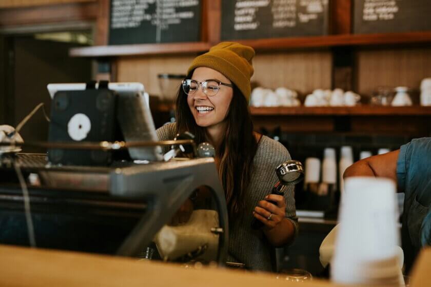 Minijob, Aushilfe / Junge Frau arbeitet als Aushilfe in einem Café und bedient die Kaffeemaschine mit einem Lächeln.