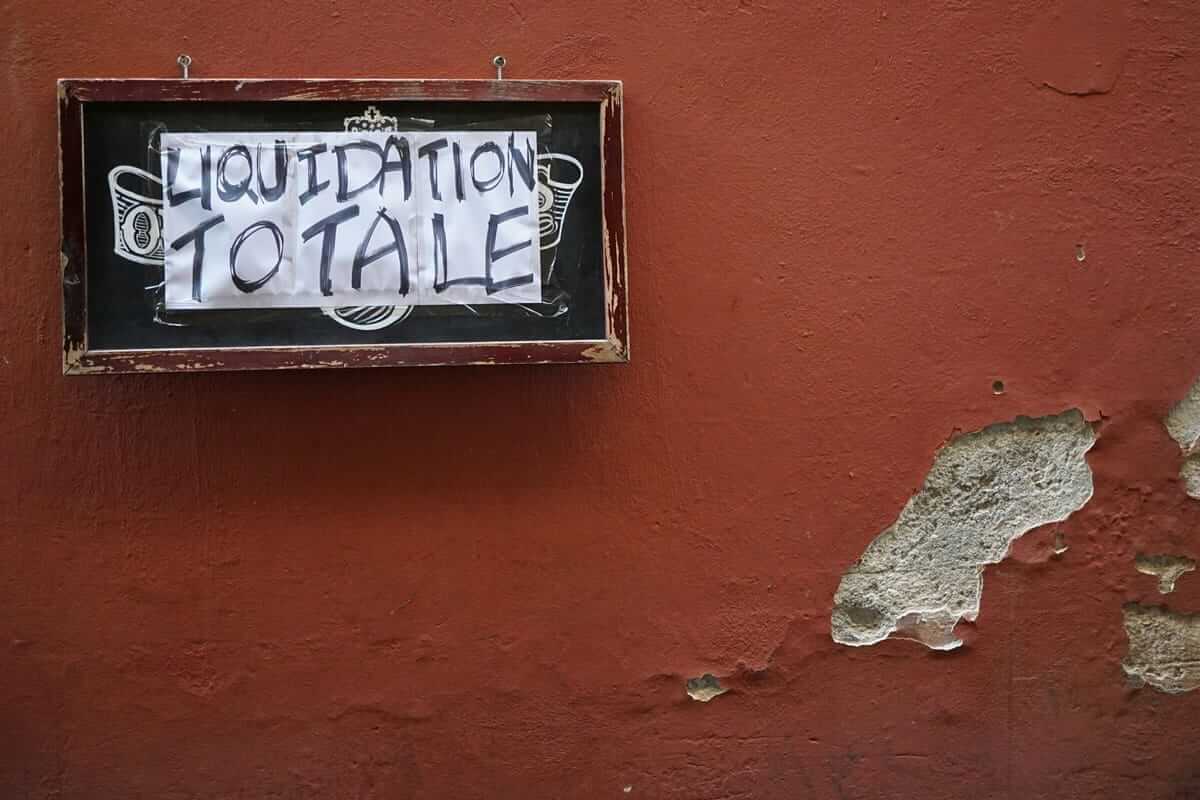 Liquidation, GMBH auflösen / Handgeschriebenes Schild mit der Aufschrift ‚Liquidation Totale‘ an einer verwitterten roten Wand – Symbol für Geschäftsauflösung und Unternehmensende
