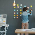 Person plant Aufgaben im modernen Büro an einer Wand mit bunten Notizzetteln – Symbol für effiziente Büroorganisation und strukturierte Arbeitsweise