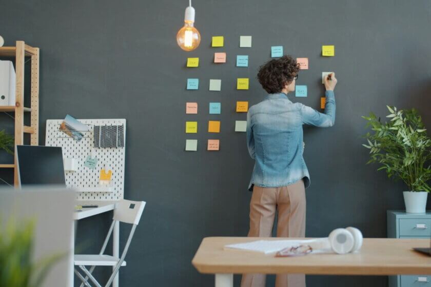 Person plant Aufgaben im modernen Büro an einer Wand mit bunten Notizzetteln – Symbol für effiziente Büroorganisation und strukturierte Arbeitsweise