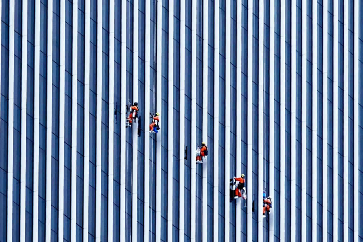 Gründen in Teilzeit: So gelingt der Weg vom Nebenerwerb zum eigenen Unternehmen Nebenerwerb / Menschen arbeiten an einer Hochhausfassade – Symbol für Stabilität, Eigeninitiative und den Weg in die Selbstständigkeit
