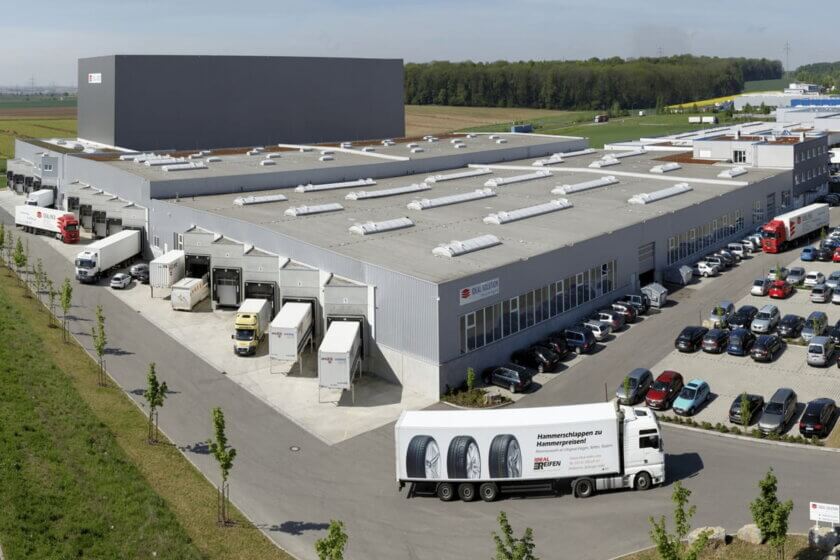 E-Commerce as a Service / Luftaufnahme des IDEAL-GROUP Logistikstandorts mit mehreren Lagerhallen, Laderampen, Lkw im Be- und Entladebereich sowie angrenzenden Parkflächen.