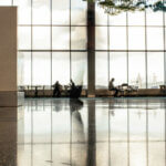 Büro am Airport / Ruhige Flughafenhalle mit großer Glasfront, vereinzelte Personen arbeiten oder warten an Tischen, sachliche und funktionale Arbeitsatmosphäre.