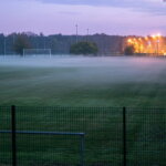 Lokales Sponsoring / Leerer Sportplatz in der Dämmerung mit Flutlicht im Hintergrund
