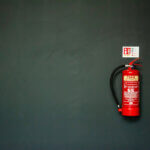 Versicherungen / Feuerlöscher an dunkler Wand – Symbol für vorbereitete Sicherheit und ruhige Vorsorge im Unternehmensalltag.