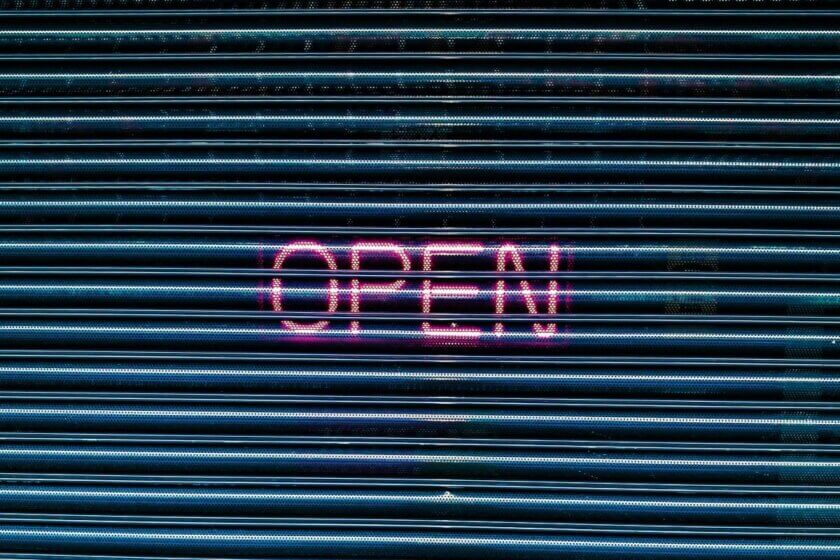Neon-Leuchtschrift "OPEN" auf einem Metall-Rolltor – Symbolbild für die Eröffnung eines Onlineshops mit dem passenden Shopsystem