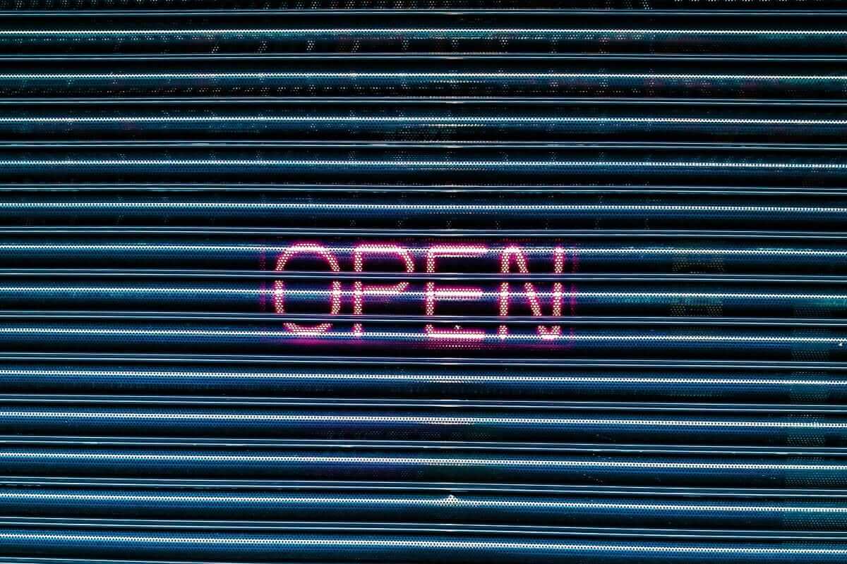 Shopsystem wählen: Welches passt zu deinem Business? (Vergleich + Checkliste) Neon-Leuchtschrift "OPEN" auf einem Metall-Rolltor – Symbolbild für die Eröffnung eines Onlineshops mit dem passenden Shopsystem
