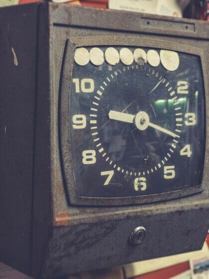 Zeitarbeit / Alte Stempeluhr an einer Wand mit Arbeitszetteln und Notizen im Hintergrund