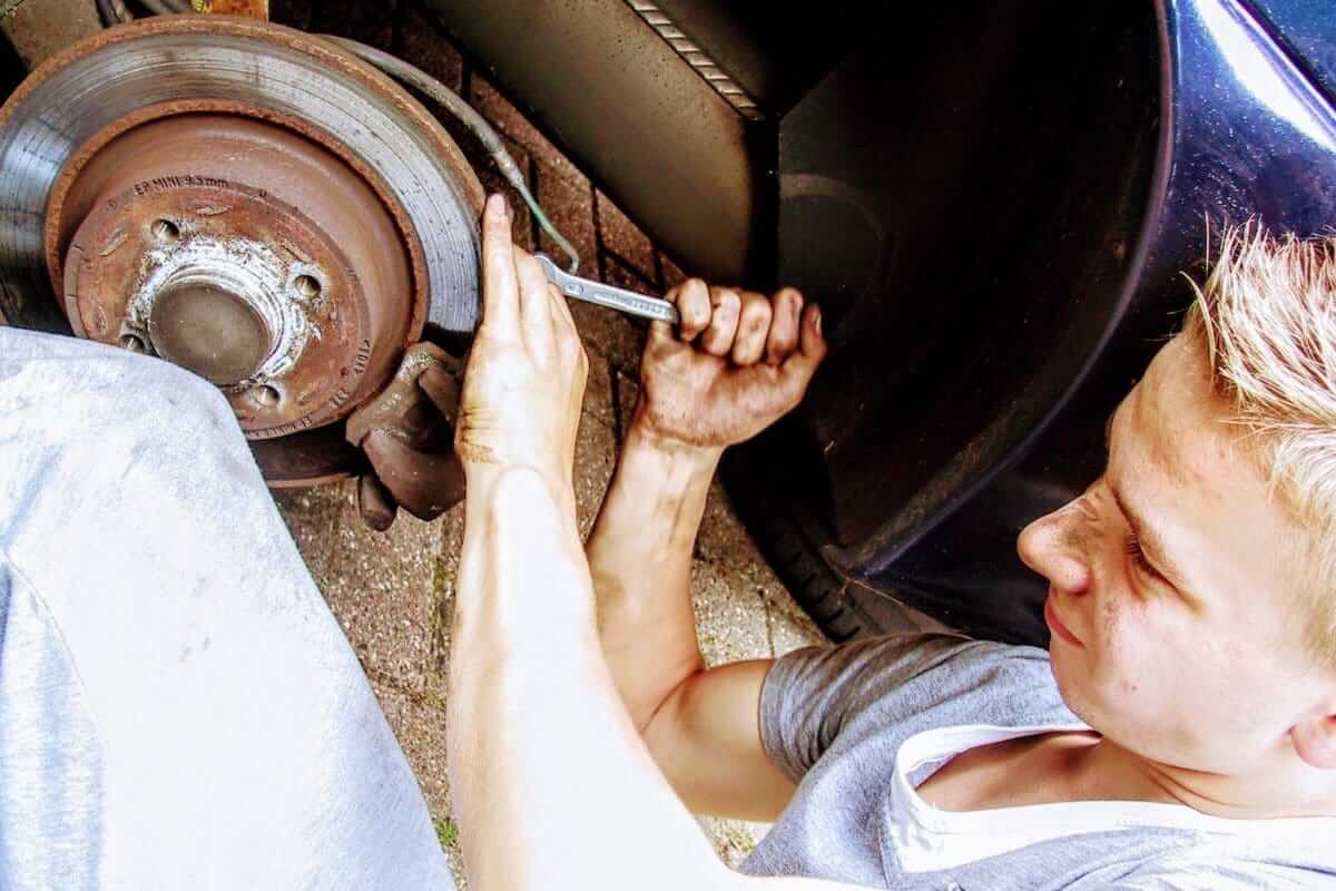 Autoreparatur (Mann repariert Bremse an Auto in Eigenregie mit Schraubenschlüssel)