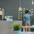 Person ordnet bunte Post-its an einer Bürowand – Organisationsstruktur im Unternehmen