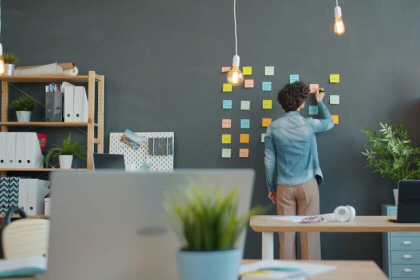 Person ordnet bunte Post-its an einer Bürowand – Organisationsstruktur im Unternehmen
