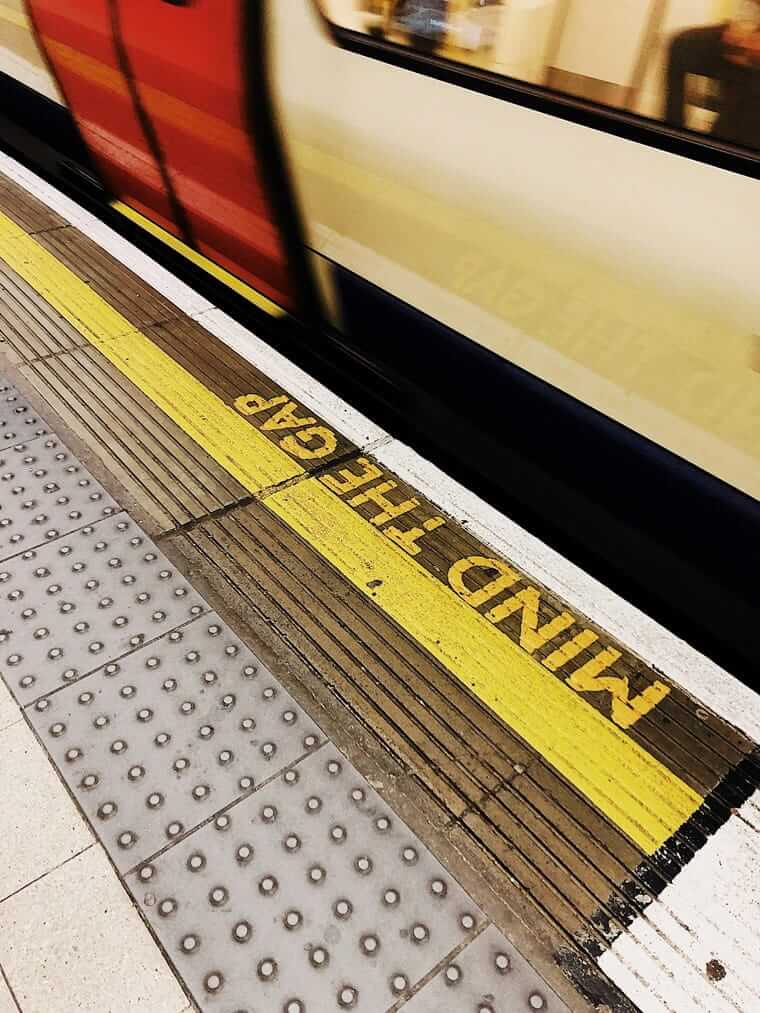 Vorbeifahrender Zug an Londoner U-Bahn-Station mit "Mind the Gap"-Schriftzug im Vordergrund — Symbol für die Rentenlücke, die entsteht, wenn man zu lange wartet