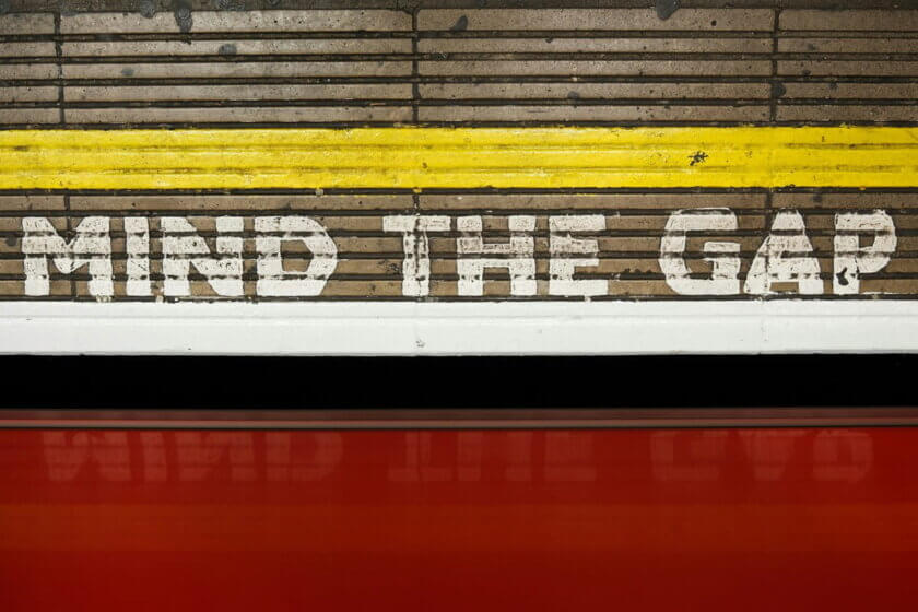 "Mind the Gap"-Schriftzug an einer Londoner U-Bahn-Wand mit rotem Waggon im Vordergrund — Symbol für die Rentenlücke bei Selbstständigen