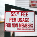 Pay-per-Use / Verwittertes Schild mit der Aufschrift „$5 Fee per Usage for Non-Members" an einem Hafengebäude – Sinnbild für nutzungsabhängige Preisgestaltung im Alltag.