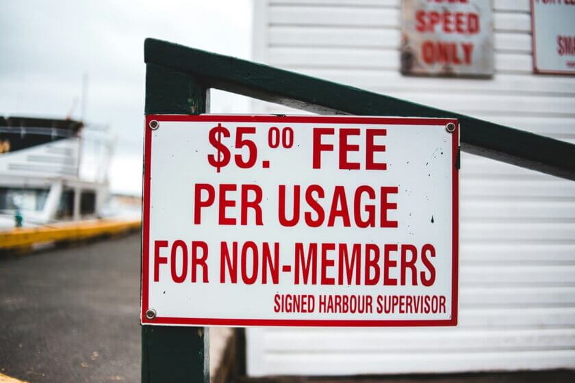 Pay-per-Use / Verwittertes Schild mit der Aufschrift „$5 Fee per Usage for Non-Members" an einem Hafengebäude – Sinnbild für nutzungsabhängige Preisgestaltung im Alltag.