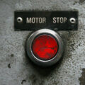 Widerrufsbutton / Roter Motor-Stop-Button auf verwitterter Betonwand mit Beschriftung Motor Stop