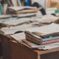 Büroorganisation / Überfüllter Schreibtisch mit gestapelten Akten und Dokumenten – Symbol für unstrukturierten Büroalltag in kleinen Unternehmen