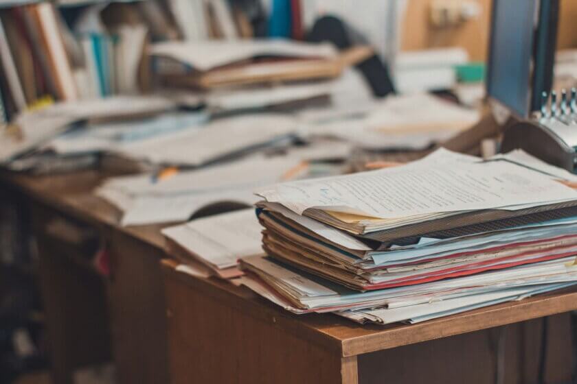 Büroorganisation / Überfüllter Schreibtisch mit gestapelten Akten und Dokumenten – Symbol für unstrukturierten Büroalltag in kleinen Unternehmen