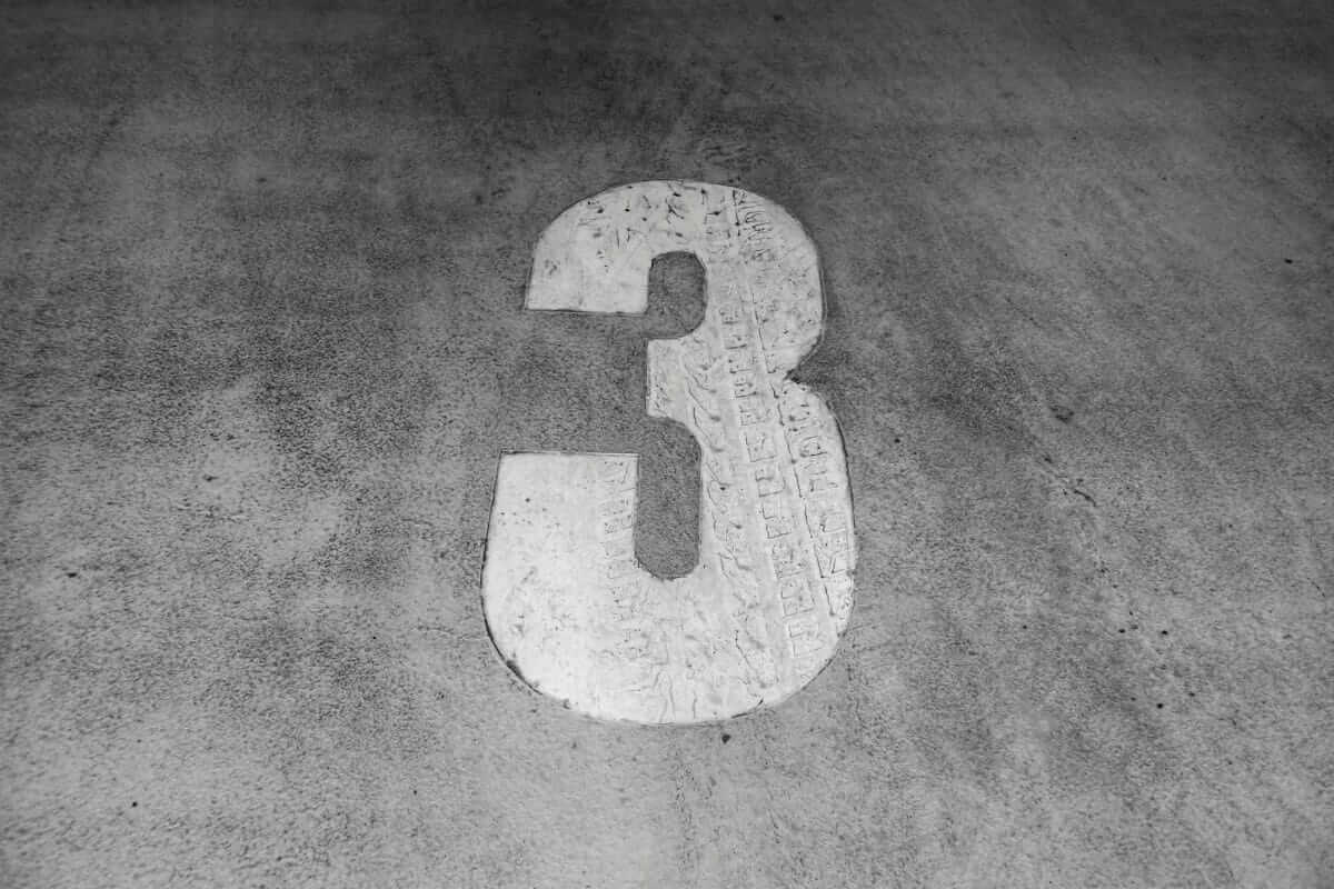 Weiße Ziffer 3 auf verwittertem Betonboden – dritter Schritt: konkrete Entscheidungen treffen.