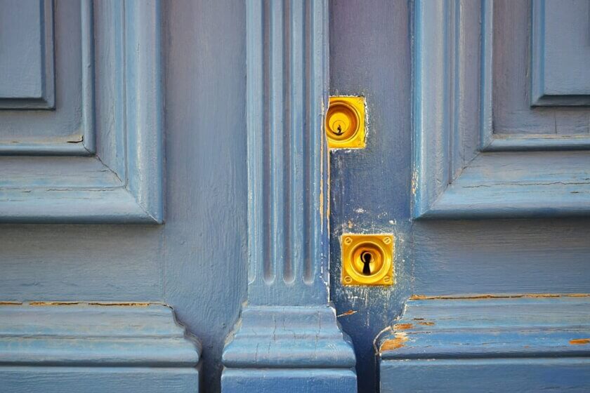 Zwei-Faktor-Authentifizierung, 2FA / Nahaufnahme einer alten blauen Holztür mit zwei übereinanderliegenden goldenen Schlössern