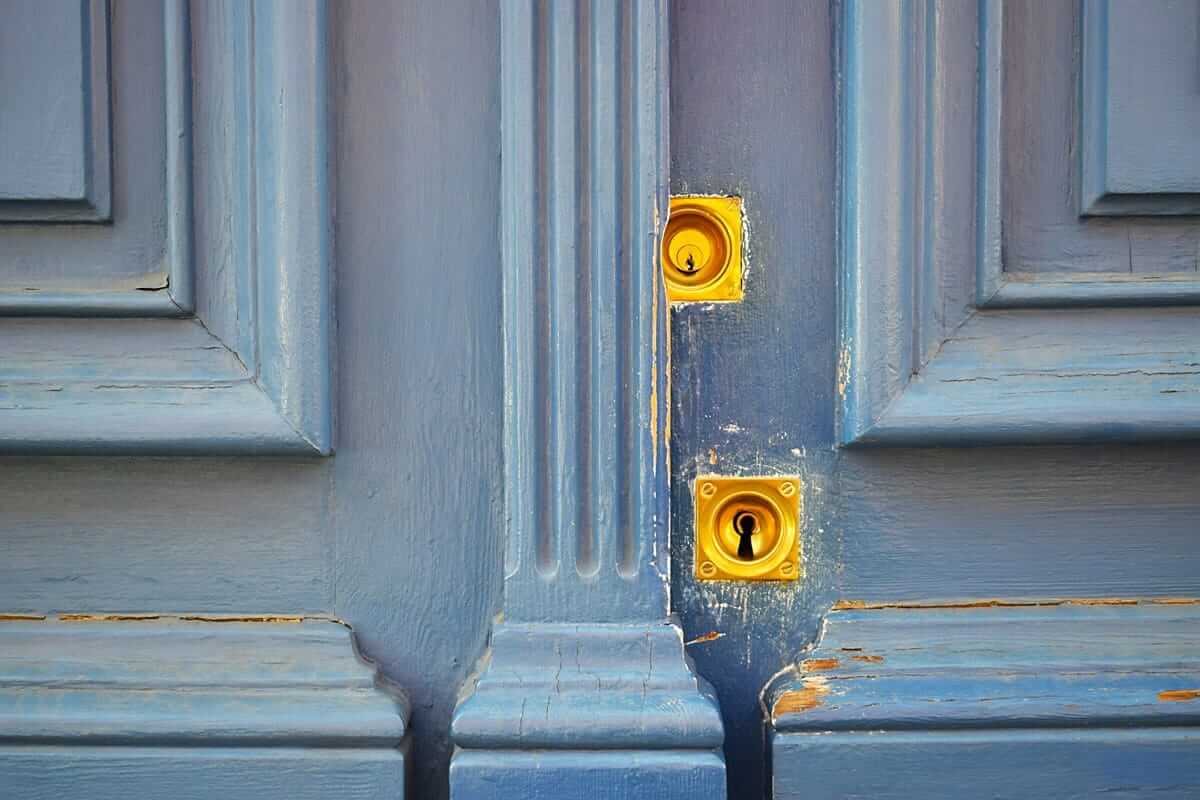 Zwei-Faktor-Authentifizierung: Warum sie unverzichtbar ist Zwei-Faktor-Authentifizierung, 2FA / Nahaufnahme einer alten blauen Holztür mit zwei übereinanderliegenden goldenen Schlössern