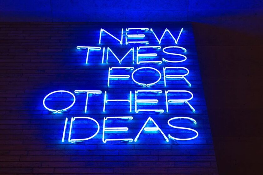 Preismodelle / Blaues Neonschild mit der Aufschrift „New Times for Other Ideas" an einer Backsteinwand – sinnbildlich für den Wandel in der Preisgestaltung und neue Monetarisierungsansätze.