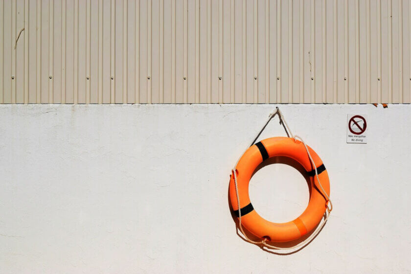 Berufsunfähigkeitsversicherung / Orangefarbener Rettungsring hängt an einer weißen Wand – Symbol für finanzielle Absicherung bei Berufsunfähigkeit.