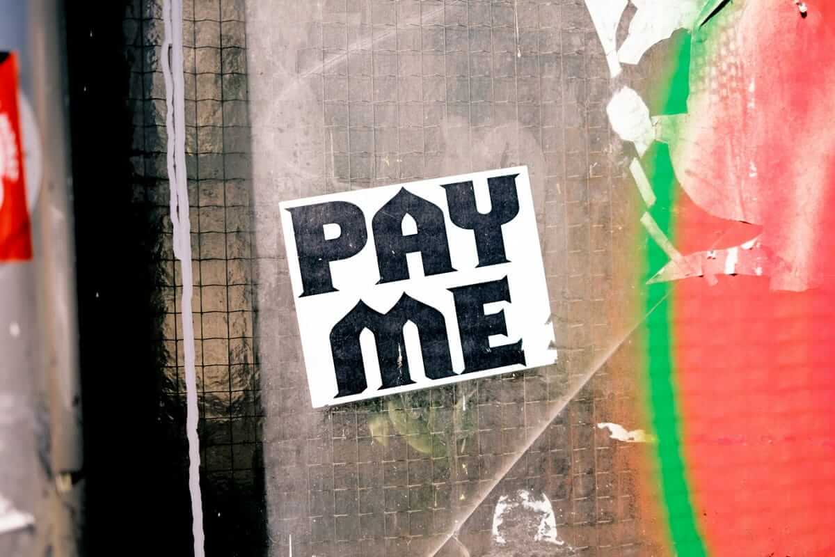 Preiserhöhung kommunizieren: So geht es ohne Kundenverlust Preiserhöhung kommunizieren / „Pay Me"-Sticker an einer Hauswand – Symbol für selbstbewusstes Preisdenken